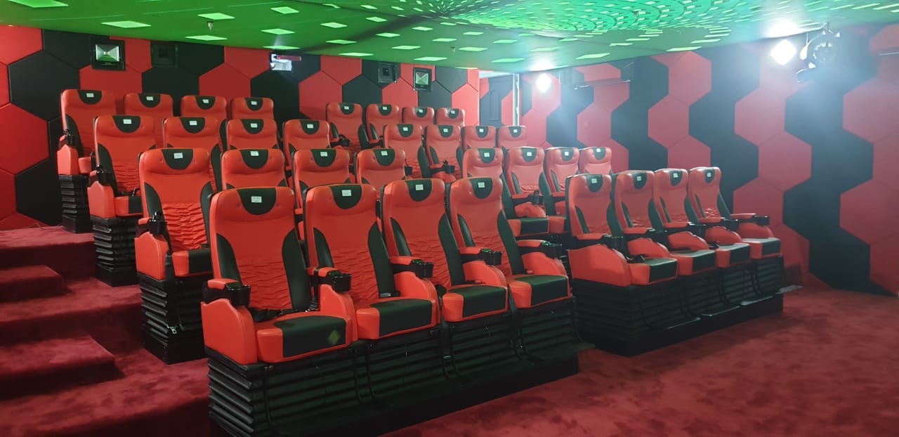 Empty 5D motion cinema inside a mall entertainment zone in Oman: rows of red and black motion seats on platform bases, hexagon-pattern acoustic wall panels, and a green LED star ceiling