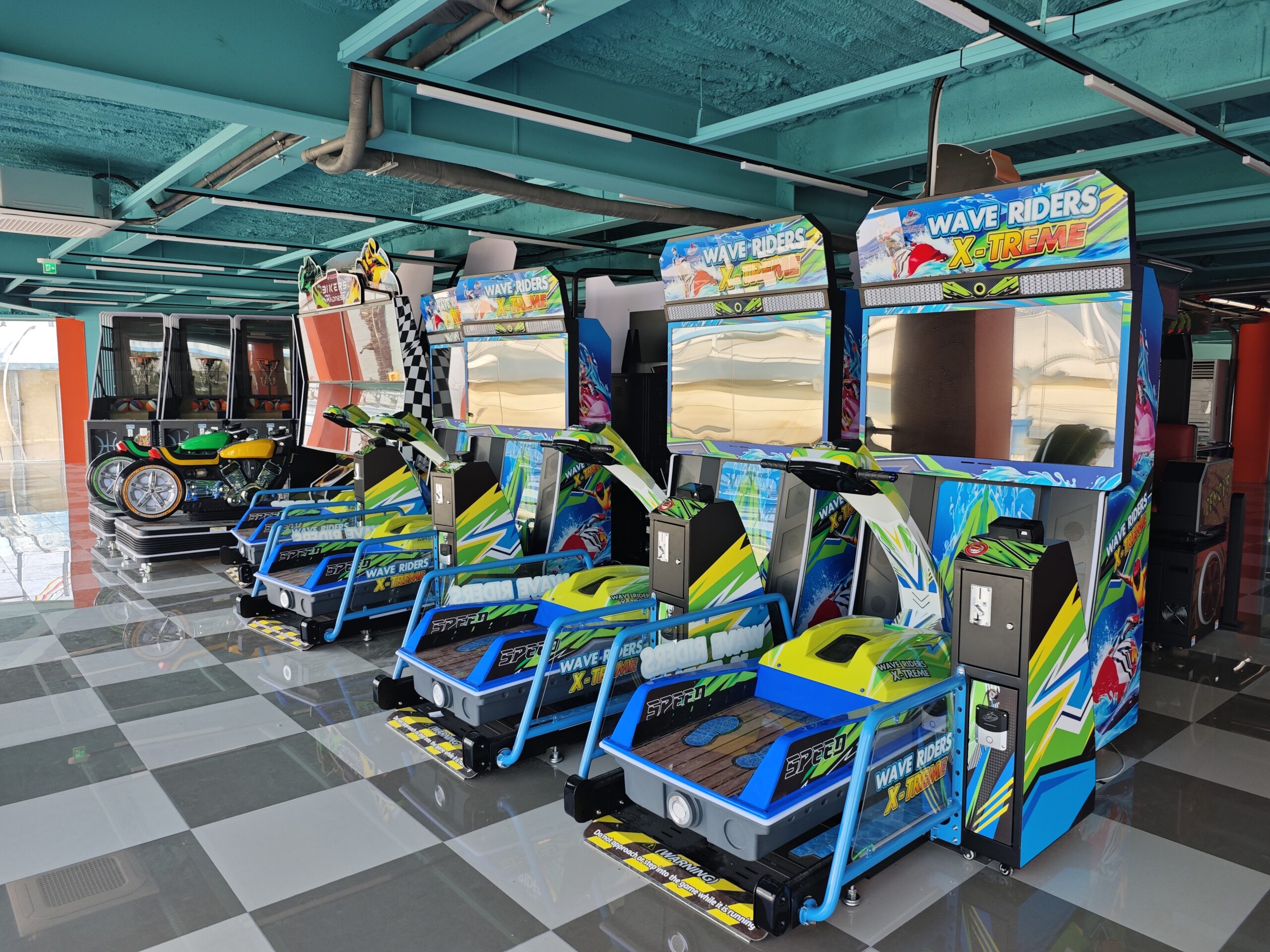 A row of jet-ski wave-rider motion simulators with a motorbike racing machine behind them, installed on a checkerboard floor in a Korean arcade dealer venue